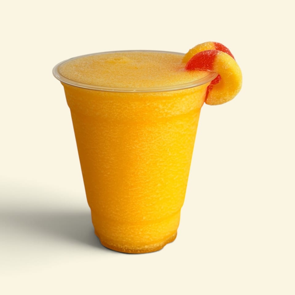 Frozen orange drink in a clear plastic cup, garnished with a red-and-yellow fruit slice against a light background.