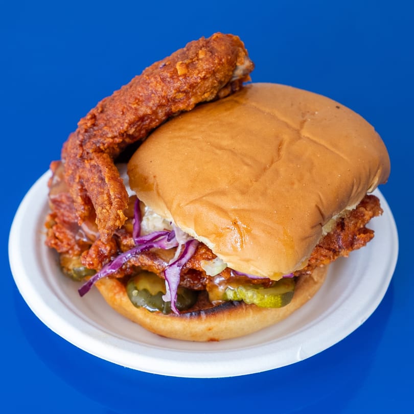 Spicy fried chicken sandwich with coleslaw and pickles, served on a white plate.