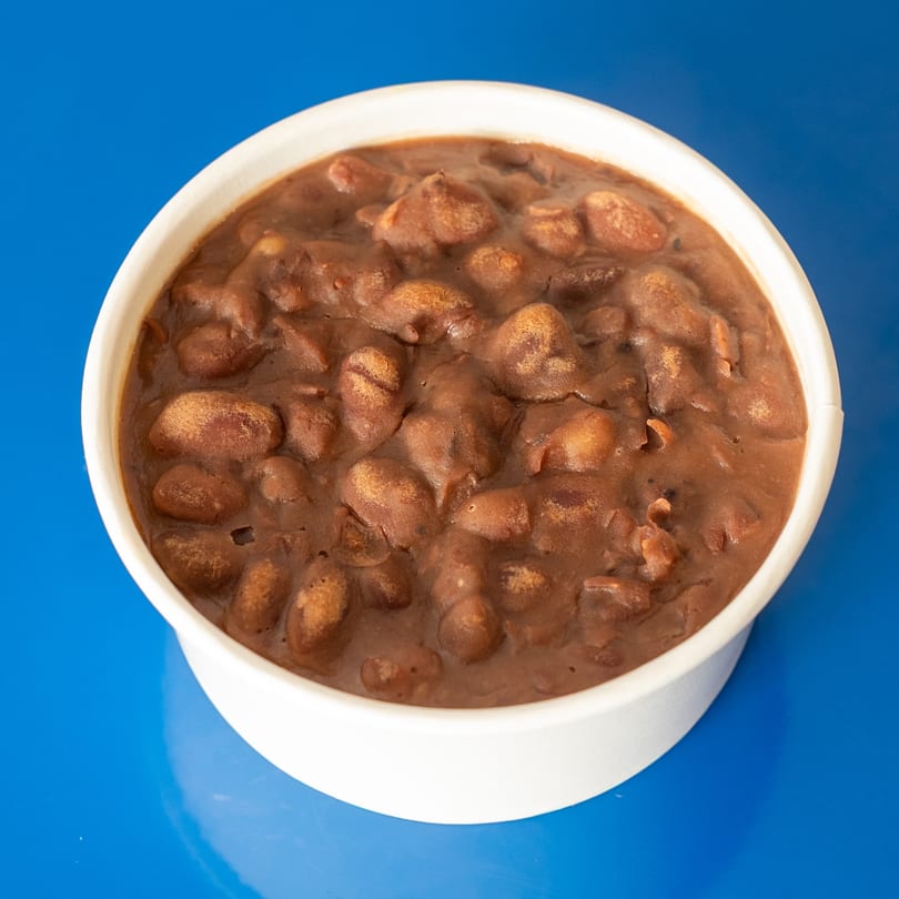A white bowl filled with dark brown refried beans, set against a vibrant blue background.