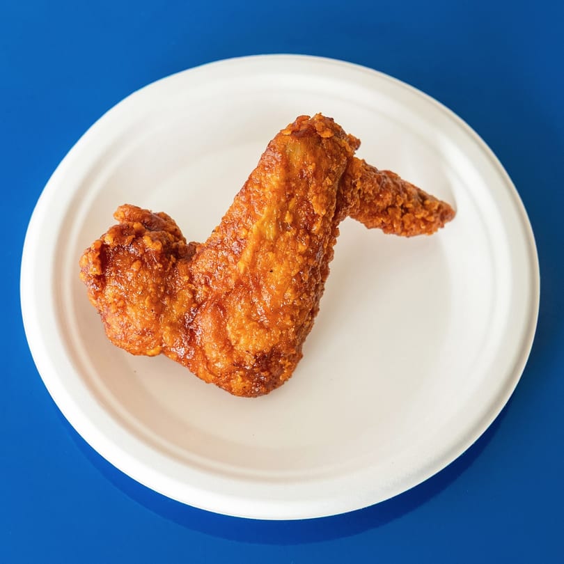 Crispy fried chicken wing on a white plate against a vibrant blue background.