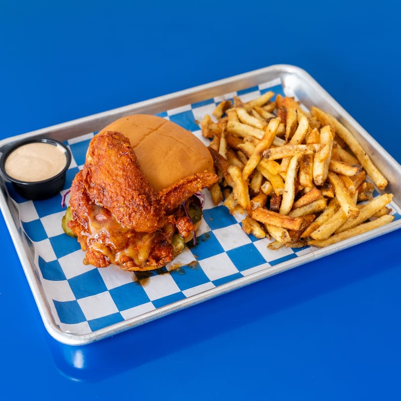 Spicy fried chicken sandwich with melted cheese, pickles, and a side of fries and dipping sauce.