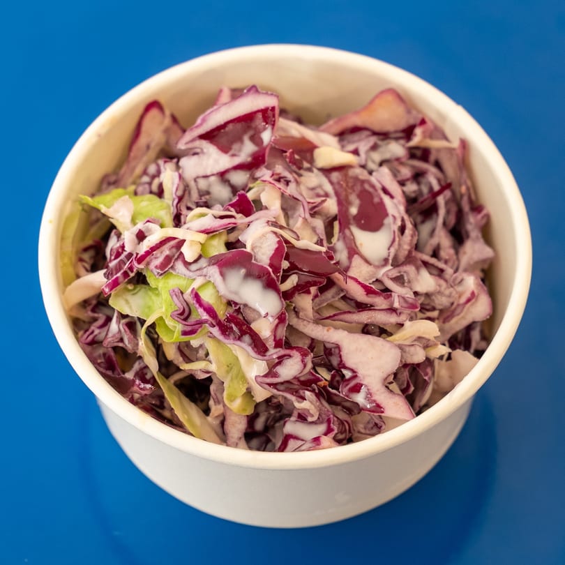 Creamy coleslaw with shredded red and green cabbage in a white bowl on a blue surface.