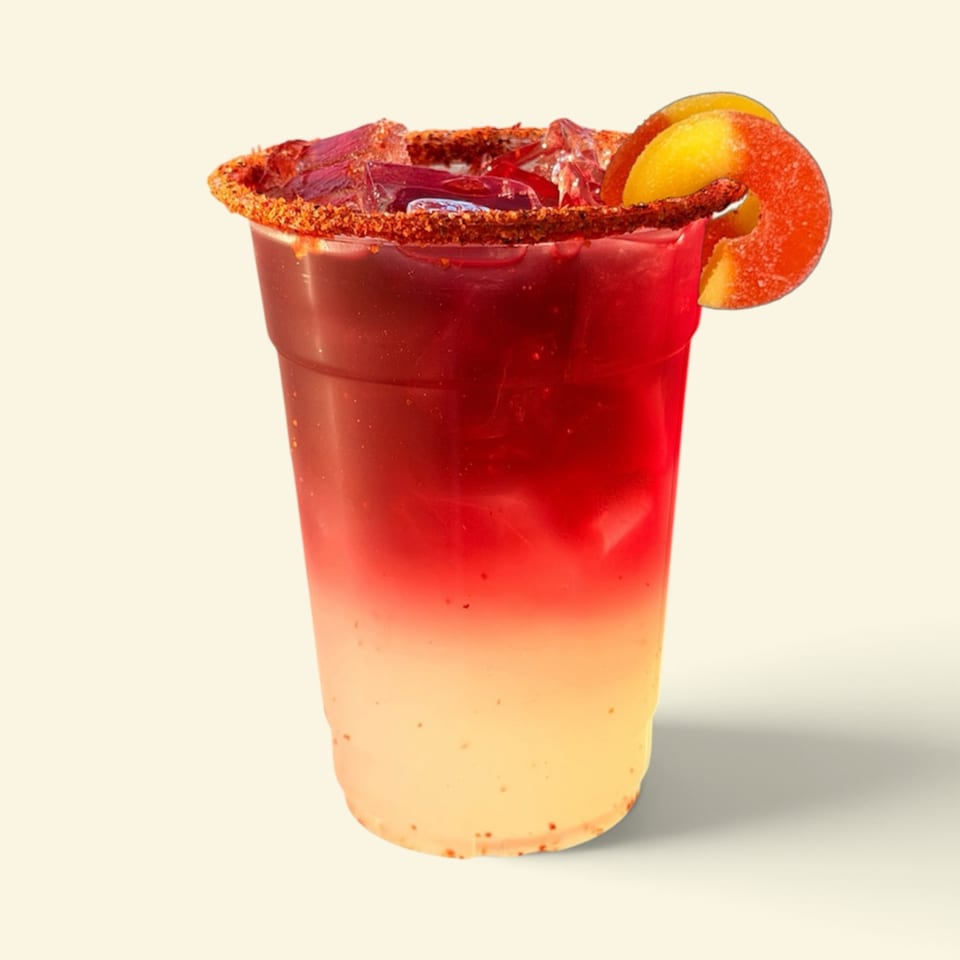 Layered red and orange cocktail in a clear cup with a chili-salt rim, citrus slices, and ice.
